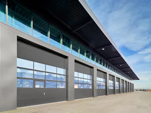 Good reasons to choose Hörmann high-speed doors and... Exterior view of a logistics hall with numerous adjacent industrial sectional doors against a blue sky