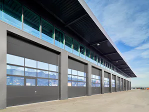 Gute Gründe für Schnelllauftore und Industrie-Sektionaltore... Außenansicht einer Logistikhalle mit zahlreichen nebeneinander liegenden Industrie-Sektionaltoren unter blauem Himmel