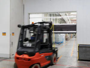 Gute Gründe für Schnelllauftore und Industrie-Sektionaltore... Schwarzroter Gabelstapler fährt auf sich öffnendes, halbtransparentes Schnelllauftor zu