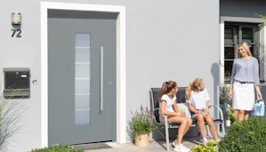 Enkele voordelen van onze Een grijskleurige voordeur ThermoSafe van Hörmann met een glasdeel in het midden. Naast de deur zitten twee kinderen op een bankje, een moeder komt aangelopen.
