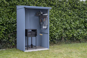 Blauwe houtopslag | Hörmann Een blauwe houtopslag van Hörmann in gebruik om onderdak te bieden aan een barbecue. De houtopslag staat op het gras in een tuin voor een struik.