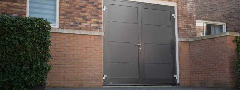 Bruinkleurig huis en aangrenzende garage met een antracietkleurige openslaande garagedeur van Hörmann