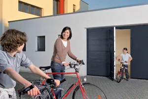 Hoe draagt een loopdeur bij aan eenvoudigere toegang tot de garage? Hörmann garagedeur met loopdeur, waar een gezin met fietsen de oprit verlaat bij een moderne witte woning.