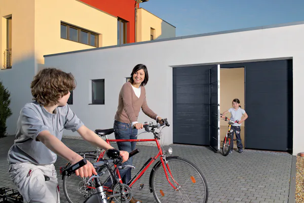 Vrouw en kinderen met fietsen voor een Hörmann garagedeur met loopdeur, één kind komt net naar buiten.