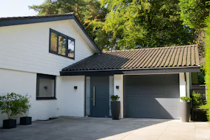 Elektrische garagedeur met loopdeur | Hörmann U ziet een modern uitziend huis met schuine daken. In het rechter deel van het huis zitten een ThermoSafe voordeur en een RenoMatic sectionaaldeur van Hörmann.