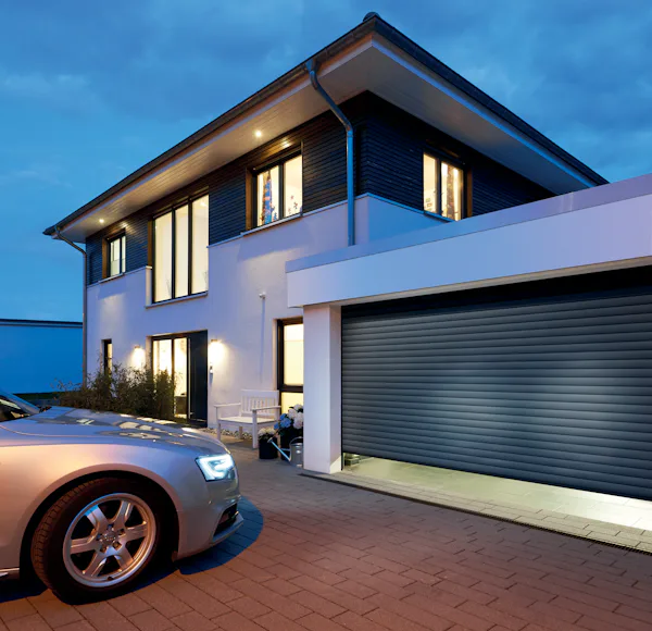 Moderne woning met gesloten Hörmann roldeur en zilveren auto op oprit bij schemering.