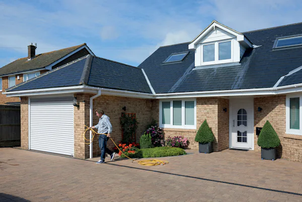 Rollmatic Roldeur | Hörmann Witte roldeur van Hörmann in een klassiek ogend huis. Op de voorgrond ziet u een man water sproeien in de voortuin.