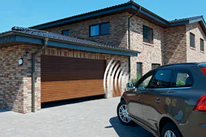 Hoe roldeuren zorgen voor efficiënter gebruik van werk- en hobbyruimtes Moderne bakstenen woning met houtkleurige Hörmann roldeur en een bruine Volvo op de oprit onder blauwe lucht.