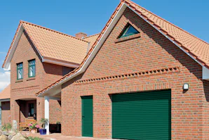 Hoe een roldeur kan bijdragen aan de uitstraling en Traditionele bakstenen woning met groene Hörmann roldeur en bijpassende zijdeur onder een pannendak.