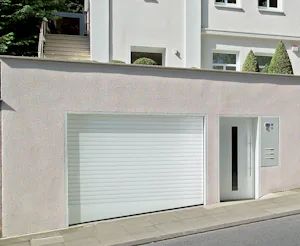 Tips voor het kiezen van de juiste elektrische garagedeur voor uw nieuwbouwwoning Witte gevel met gesloten witte Hörmann roldeur direct aan de straat, zonder zichtbare oprit.