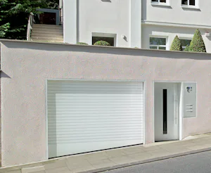 Tips voor het kiezen van de juiste elektrische garagedeur voor uw nieuwbouwwoning Witte gevel met gesloten witte Hörmann roldeur direct aan de straat, zonder zichtbare oprit.