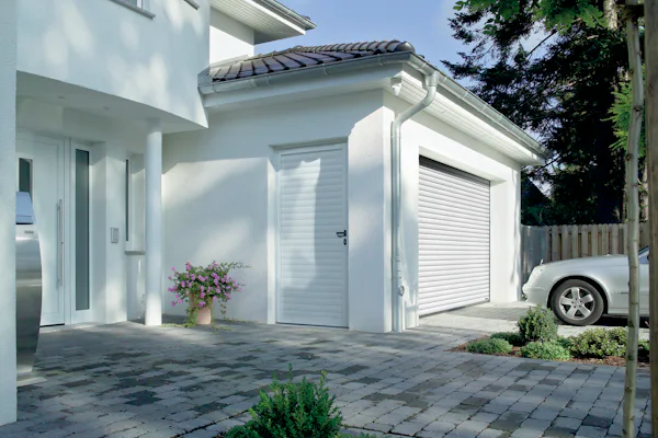 Witte woning met gesloten witte Hörmann roldeur en zijdeur, grijze auto op de oprit en nette voortuin.