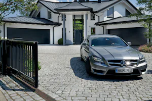 Voordelen van een veilige roldeur voor Luxe villa met drie zwarte Hörmann roldeuren, een open poort en een zilveren Mercedes op de kasseien oprit.