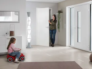 ThermoSafe voordeur | Hörmann Kind zit op een loopauto in de hal van een huis. Moeder loopt net door een deur de hal in.