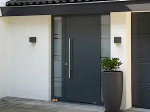 Extra opties voor de Een antracietkleurige ThermoSafe voordeur, is matchend met de garagedeur ernaast. Naast de deur staat een pot met een plant erin.