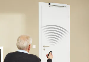 Elektrische deuropener | Gemakkelijk met afstandsbediening Elektrische deuropener met afstandsbediening - Een oudere man bedient een witte binnendeur met een afstandsbediening. De deur is voorzien van een elektrische deuropener, geïllustreerd door radiogolven op de deur. Het systeem is ontworpen voor gemakkelijke toegang en gebruiksvriendelijkheid, vooral voor mensen met beperkte mobiliteit.
