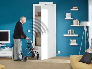 Oft sind es die kleinen Dinge, die den Alltag erleichtern... Älterer Herr mit Rollator öffnet Tür bequem mittels Knopfdruck