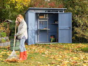 Mit dem gewissen Extra wird Ihr Gerätehaus noch ein bisschen... Frau recht herbstliches Laub vor einem blauen Gerätehaus von Hörmann