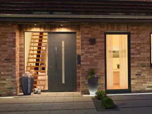 De ultieme Hörmann ThermoSafe Hybrid voordeur in donkergrijs met verticale glasstrook, naast trap en verlichte entree met planten.