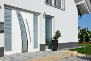 Uitstekende warmte-isolatie Witte Hörmann ThermoSafe Hybrid voordeur met gebogen glasaccent, zijlichten en hoge plantenbak bij modern huis.