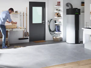 Functionele deur H3 OD Een man is bezig met werkzaamheden aan een houten object op een werkbank. Hiernaast ziet u een MZ Thermo deur van Hörmann die toegang biedt tot de tuin.