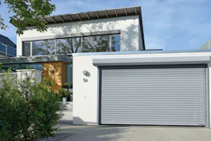RollMatic T Wit modern huis met een grijskleurige garage roldeur van Hörmann. Links onder en boven ziet u begroeiing.