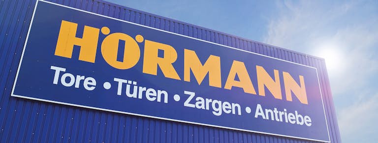 Het logo van Hörmann op een blauw pand met een zonnige lucht.
