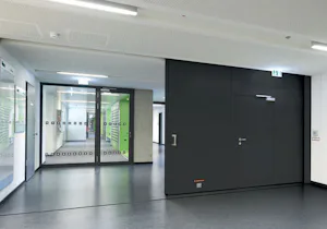 Automatische sluitmechanismen en sensoren
Optionele... Antracietkleurige brandwerende schuifdeur van Hörmann. Deze schuifdeur staat in een verzamelgebouw in de hal.