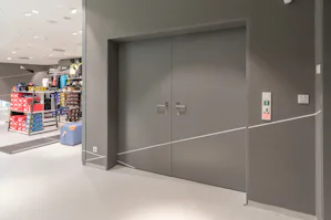 Grijze functionele binnendeuren Stijlvolle grijze Hörmann binnendeur met dubbele deuren en moderne handgrepen, geïntegreerd in een commerciële winkelomgeving met sportartikelen en veiligheidsbediening aan de rechterzijde