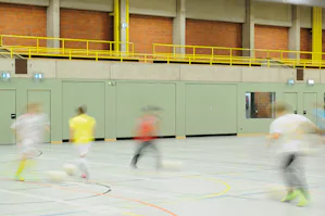 Voor onze sporthaldeuren staat veiligheid centraal. De... Personen spelen in een sporthal, in de wand zijn sporthaldeuren van Hörmann ingebouwd.