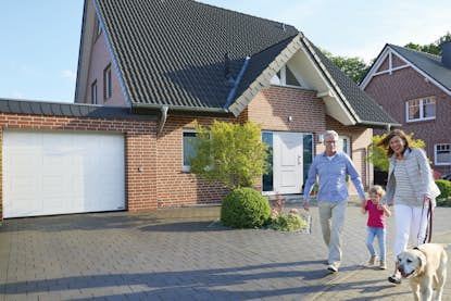 Familie mit Hund vor einem Haus mit sicherer Haustür und einem Garagentor Familie mit Hund vor einem Haus mit sicherer Haustür und einem Garagentor