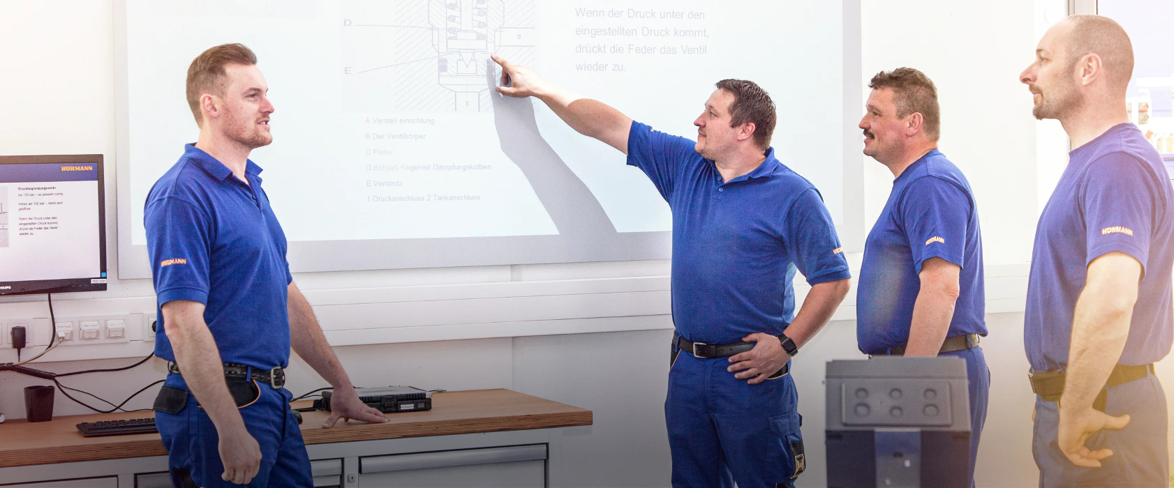 Vier medewerkers van Hörmann overleggen aan de hand van een powerpoint presentatie.