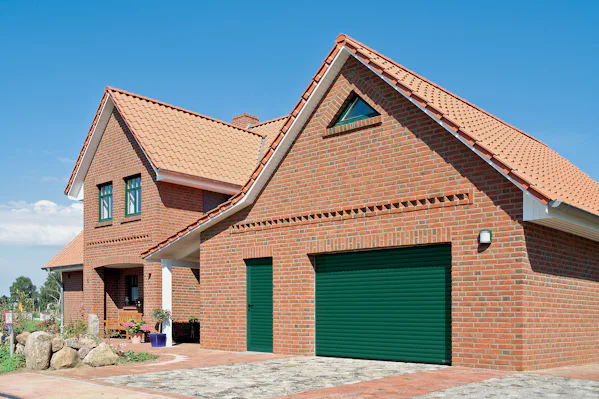 Een groene garageroldeur in een grote, lichtbruine woning.