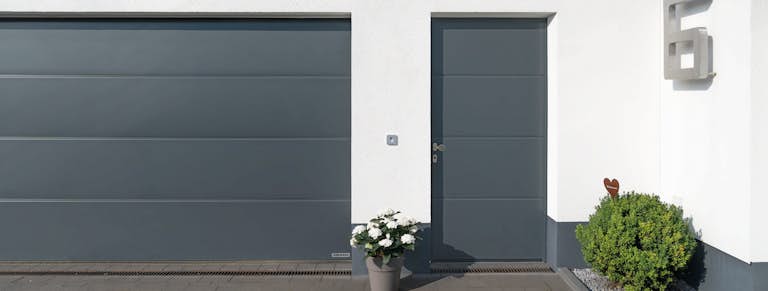 Vit fasad med grå garageport och matchande sidodörr.