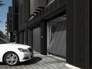 Behovet av parkeringsplatser i storstäder och tätorter ökar... Vit bil väntar på att en svart port till ett parkeringsgarage ska öppna sig.