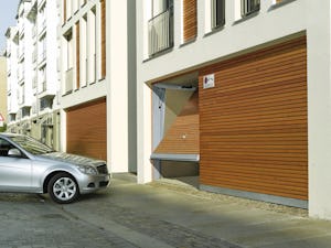 Behovet av parkeringsplatser i storstäder och tätorter ökar... Port beklädd med träpanel öppnar sig för att släppa in en bil i parkeringsgaraget.