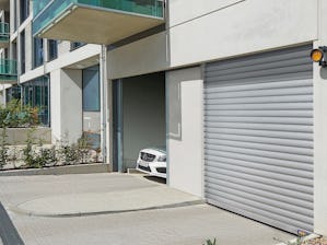 Behovet av parkeringsplatser i storstäder och tätorter ökar... En bil kör ut genom utfarten från ett parkeringsgarage. bredvid är infarten, där är porten stängd.