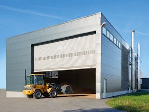 Hörmann rullportar och rullgaller i aluminium och stål är... En port öppnar sig så en gul traktor med skopa kan köra in.